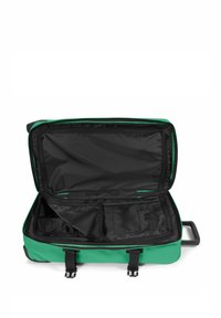 Grön resebag med ett stort öppet fack, svart inredning, svarta dragkedjefickor och dubbla remstängningar.