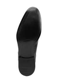 Suela de zapato negra con superficie de goma texturizada, que presenta un perímetro liso y una marca en relieve. Diseño plano para un soporte estable.
