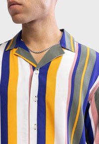 Chemise à manches courtes présentant des rayures verticales bleues, jaunes, grises, roses et blanches. Boutonnage sur le devant et col en V.