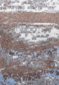 Gros plan sur un tissu tricoté doux avec un motif aux couleurs marron, gris, bleu et blanc atténuées montrant des fibres de laine texturées.