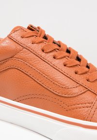 Baskets en cuir orange avec empeigne texturée, lacets noirs contrastants et semelle intermédiaire blanche avec une fine ligne d'accent rouge.