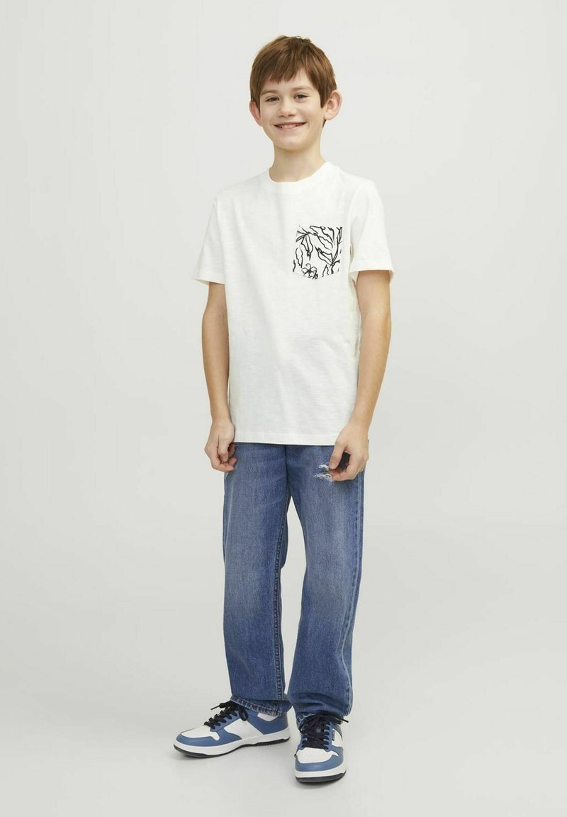 White cotton t-shirt with a black abstract patterned pocket, paired with blue straight-leg jeans and blue and white sneakers.