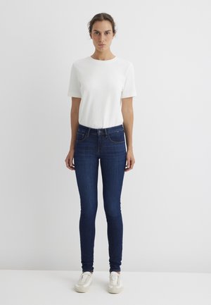 White short-sleeve t-shirt paired with dark blue skinny jeans. Outfit features a simple design and smooth texture. Footwear is light-colored sneakers.