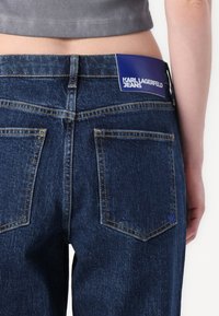 Donkerblauwe denim jeans met een hoge taille, voorzien van twee achterzakken en een zichtbaar blauw label met de branding "KARL LAGERFELD JEANS."