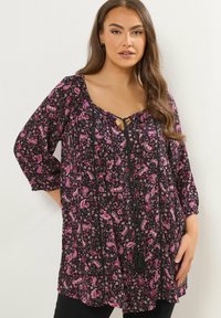 Tunica nera con motivo paisley rosa, presenta una scollatura a forma di cuore con un laccio, maniche a 3/4 e una vestibilità ampia. Dettagli neri e nappina.