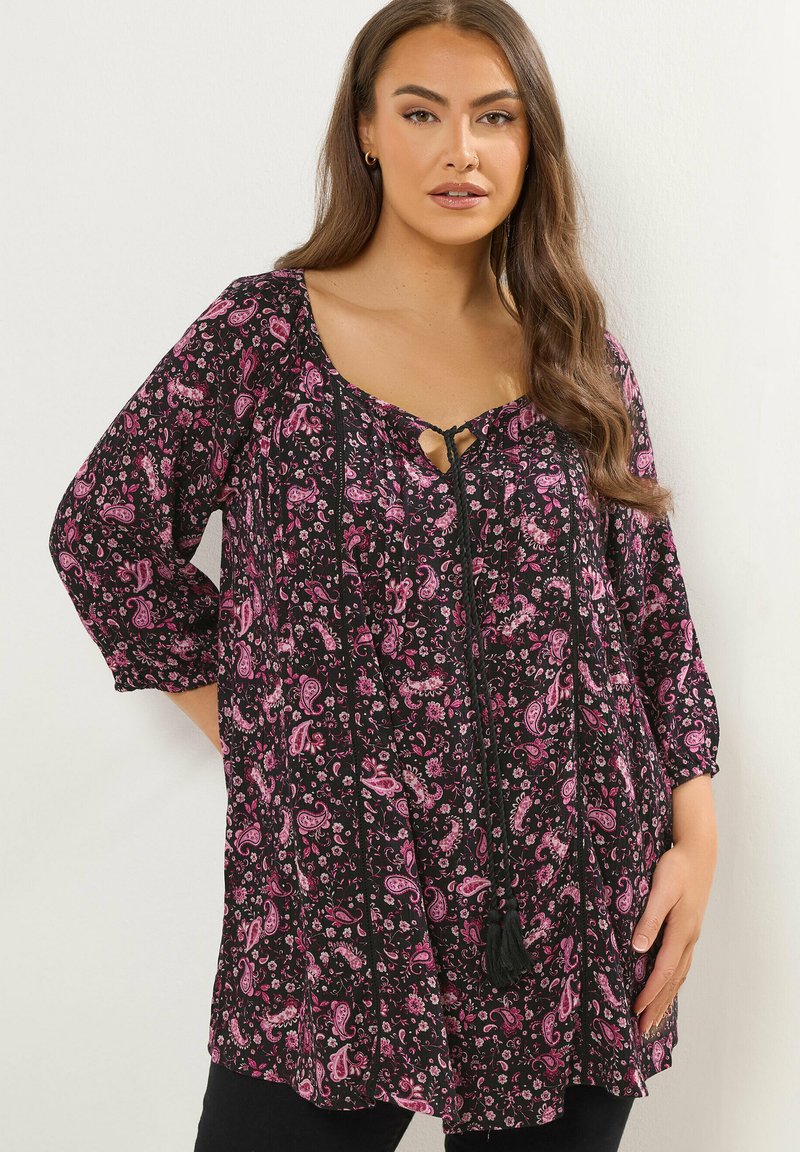 Tunica nera con motivo paisley rosa, presenta una scollatura a forma di cuore con un laccio, maniche a 3/4 e una vestibilità ampia. Dettagli neri e nappina.