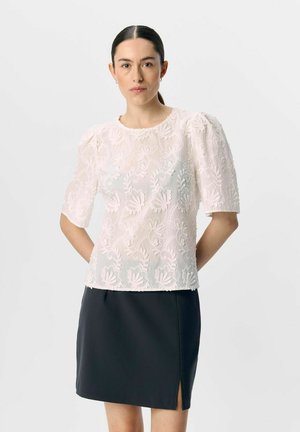 Blusa blanca bordada con mangas abullonadas, con un diseño floral, combinada con una falda mini negra con una abertura lateral. Textura suave, tela ligera.