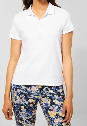 Witte korte mouw polo met kraag. Gladde katoenen textuur. Gecombineerd met kleurrijke broek met bloemmotief in blauw, roze en geel.