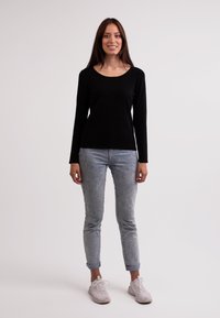 Schwarzes Langarmshirt, taillierter Schnitt, kombiniert mit hellblauen, umgeschlagenen Skinny-Jeans und grauen Sneakers mit strukturierter Oberfläche.