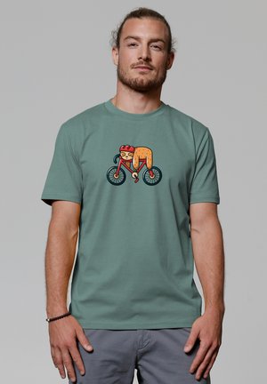 Green cotton t-shirt with a cartoon design of a cycling animal. The animal is wearing a helmet and the bike has black wheels.