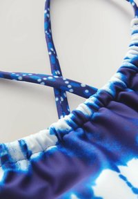 Horečkový vrch s modro-bielym tie-dye vzorom, ktorý má tenké nastaviteľné ramienka a zbrúsenú látku okolo výstrihu.