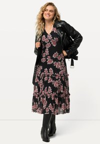 Vestido maxi negro con flores rosas, volantes y capas; combinado con una chaqueta de cuero negra y botas negras hasta la rodilla.
