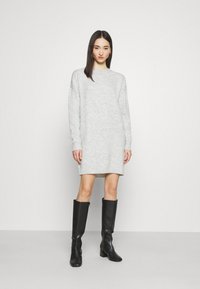 Abito grigio a maglia con maniche lunghe, vestibilità rilassata e scollatura arrotondata. Abbinato a stivali neri con tacco al ginocchio. Design semplice e con texture.