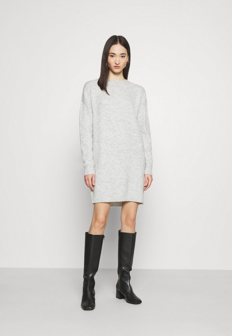 Abito grigio a maglia con maniche lunghe, vestibilità rilassata e scollatura arrotondata. Abbinato a stivali neri con tacco al ginocchio. Design semplice e con texture.
