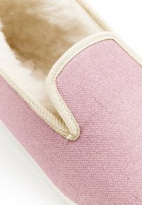 Pantofole rosa con una tomaia in tessuto texturizzato, una morbida fodera in pelliccia e dettagli beige lungo i bordi.