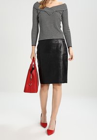 Gonna a matita in pelle nera abbinata a un top a spalle scoperte a righe bianche e nere. Gli accessori includono una borsa rossa e tacchi alti rossi.