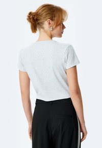 Lys grå, kortærmet ribbet t-shirt med rund hals, bæret med højhalsede sorte bukser, der viser et enkelt og tætsiddende design.
