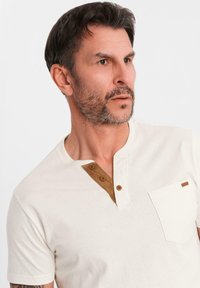 Pánská polokošile s krátkým rukávem v barvě off-white z bavlny, s hnědým akcentem na límci, tříknoflíkovou légou a náprsní kapsou.