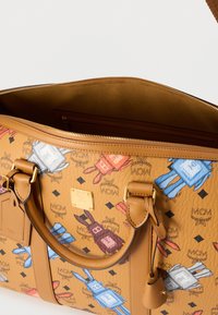 Bolso de mano MCM de cuero color canela con estampado de conejos coloridos, herrajes dorados, asas dobles y cremallera abierta que muestra un bolsillo interior.
