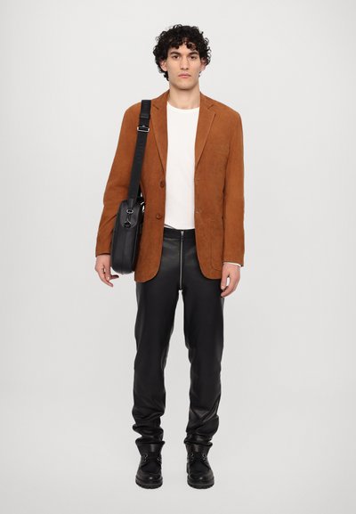 Brown suede blazer, white textured sweater, black leather pants, and black boots. Model also carries a black crossbody bag.