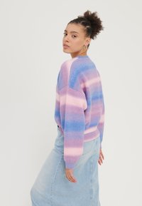 Purple and pink striped sweater with a relaxed fit, ribbed hem and cuffs, worn over a light denim skirt. Soft texture and knit material.