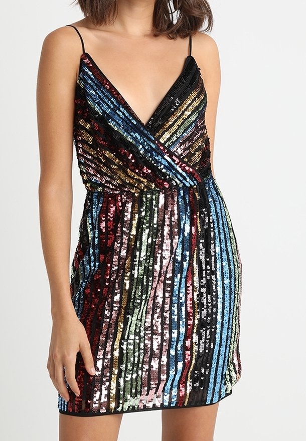 Frau, die ein ärmelloses, V-ausschnitt Mini-Kleid mit vertikalen, mehrfarbigen Paillettenstreifen und dünnen schwarzen Schulterträgern trägt.