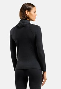Black, ribbed long-sleeve top with a fitted shape and a hood. Features seamless design with textured fabric and thumbholes on the cuffs.