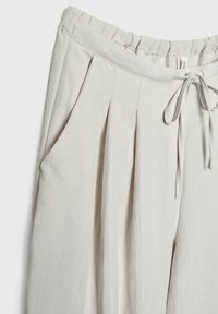 Pantalon beige clair avec taille élastique, cordon de serrage et plis sous la taille sur fond uni.