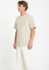 Beige katoenen t-shirt met een ontspannen pasvorm, korte mouwen en een klein zwart logo op de borst, gecombineerd met witte cargobroeken.