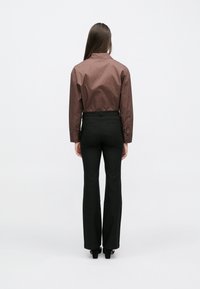 Chemise marron à manches longues avec un col montant, associée à un pantalon noir ajusté. La tenue présente une texture lisse et un design minimaliste.