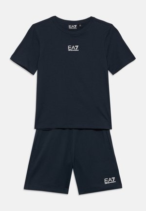 Granatowy zestaw składający się z krótkiego t-shirtu z krótkim rękawem i szortów, każdy z białym logo EA7 Emporio Armani na środku przodu i na dolnej lewej stronie.