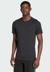 Čierne športové tričko s okrúhlym výstrihom, s raglánovými rukávmi a diskrétnym čiernym logom na hrudi. Vyrobené z hladkej tkaniny.