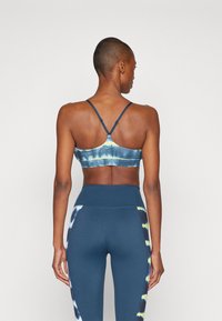 Sutiã desportivo em tie-dye azul-marinho com alças finas e um design justo, combinado com leggings de cintura alta que apresentam detalhes laterais em azul e amarelo.