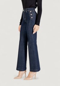 Jeans a vita alta e gamba larga in denim blu scuro, caratterizzati da dettagli in metallo dorato sui lati, completati da una texture liscia.