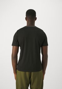 Mustad lühikeste varrukatega t-särk ümmarguse kaelusega ja siledat tekstuuri, vaadatuna tagant. Kantud oliiviroheliste pükstega, minimalistliku disainiga.