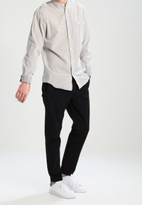 Camicia a maniche lunghe, con bottoni, a righe verticali bianche e grigie; abbinata a pantaloni neri e sneakers bianche. Design semplice e classico.