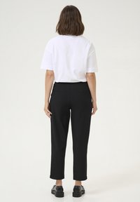 T-shirt bianco a maniche corte e pantaloni neri sartoriali con tasche posteriori, tagliati alla caviglia, abbinati a scarpe chunky nere. Design semplice.