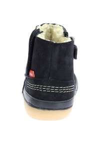 Bota de ante negra con forro de felpa, detalles cosidos y suela de goma. Presenta una etiqueta roja en el lateral y un cierre trasero seguro.