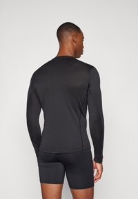 Schwarzes langärmliges Sportoberteil mit strukturiertem Muster, kombiniert mit schwarzen figurbetonten Shorts. Nahtdetails entlang der Ärmel und des Saums.