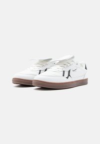 Λευκά αθλητικά παπούτσια με συνθετικό επάνω μέρος, διακοσμημένα με μαύρο λογότυπο και καφέ λαστιχένια σόλα. Διαθέτουν παραδοσιακό κορδόνι για σταθερό κράτημα.