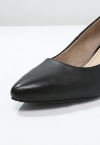Svarta läderpumps med spetsig tå, slät yta, minimalistisk design och låg klack. Inredningen har en beige foder.