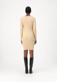 Abito a maglia a coste beige con maniche lunghe, silhouette aderente e scollatura a barca, abbinato a stivali neri in pelle con tacco al ginocchio.