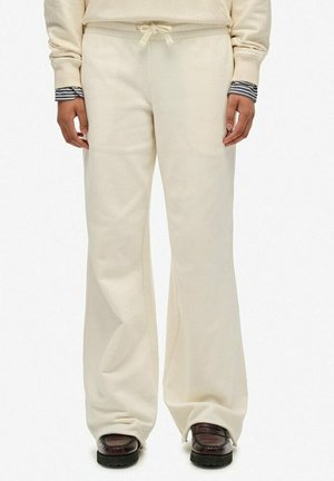 Person wearing cream-colored drawstring pants with wide legs and dark brown loafers, hands relaxed at sides against a white background.