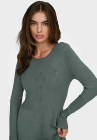 Robe à manches longues en maille côtelée dans un vert muted, avec un haut ajusté, un bas évasé et une texture subtile, dotée d'un col rond et de passages pour les pouces.