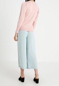 Pull à manches longues de couleur rose clair avec une finition texturée, associé à un pantalon large style culotte bleu clair, et des chaussures noires à talons blocs.