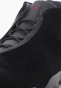 Czarne zamszowe buty do koszykówki z czarnymi sznurówkami, skórzanym językiem i czerwonym logo Jumpman na języku, szara podeszwa widoczna na dole.