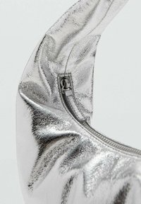 Srebrna metalna torbica z teksturirano površino, ukrivljenim dizajnom in vidnim zadrgo. Poudarja elegantne, odbojne površinske detajle.