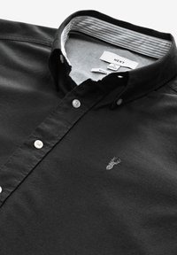 Camicia nera con bottoni in cotone, caratterizzata da una texture liscia, con colletto, bottoni bianchi e un piccolo logo argentato sul petto.