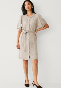 Beige, gebreide jurk met korte pofmouwen, knopen aan de voorkant en een gevlochten tailleband. Zachte textuur en een knie-lange ontwerp met ribgebreide randen.