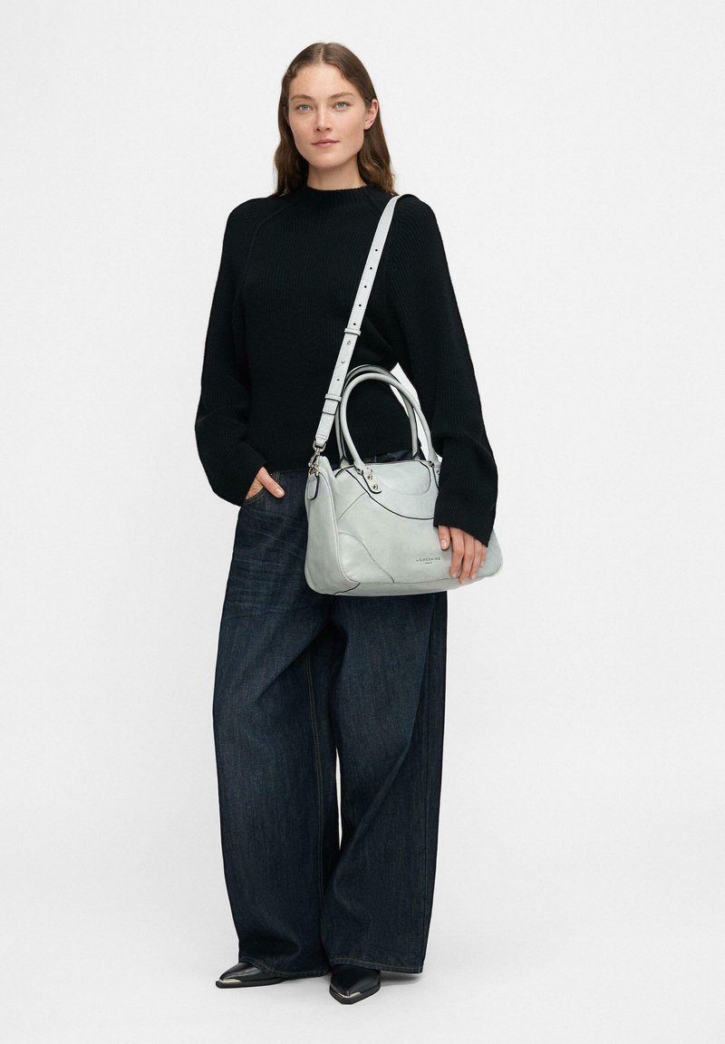 Szara skórzana torebka z podwójnymi uchwytami, regulowanym paskiem, gładką fakturą i zaokrąglonym kształtem, w połączeniu z czarnym swetrem i spodniami o szerokich nogawkach.